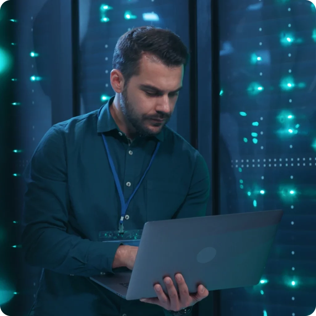 En cybersikkerhetsekspert analyserer data på en bærbar datamaskin i et høysikkerhets serverrom, som viser Energinets robuste databeskyttelsestiltak.
